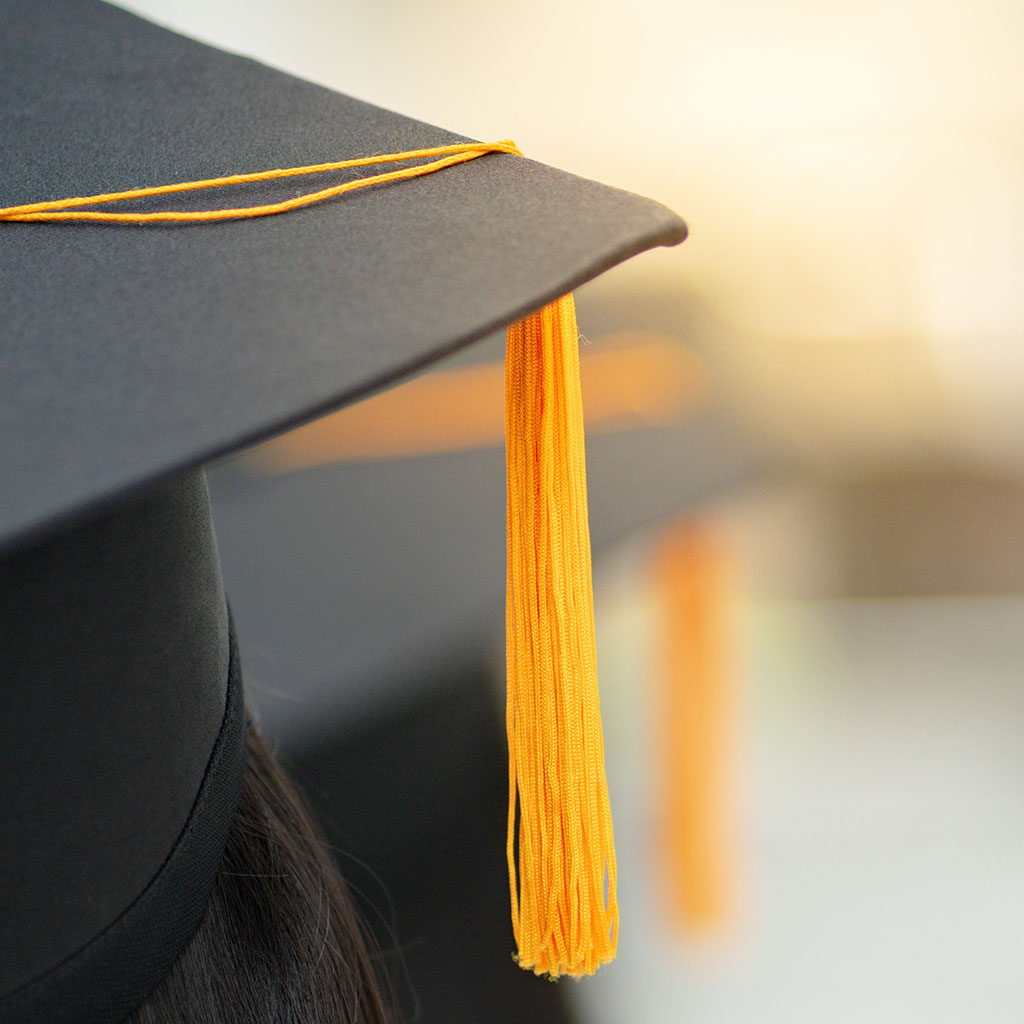 Young happy Asian woman university graduate in graduation gown a Jacksonville College crosses